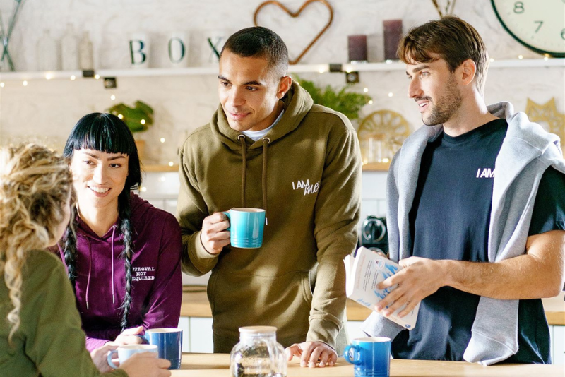 A group of friends gathered around a kitchen island chatting and drinking cups of tea and coffee